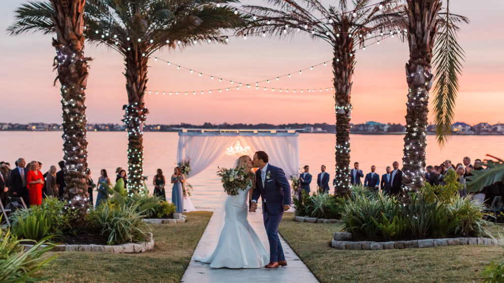 Wedding couple at the edge of the lake with string lights above them.