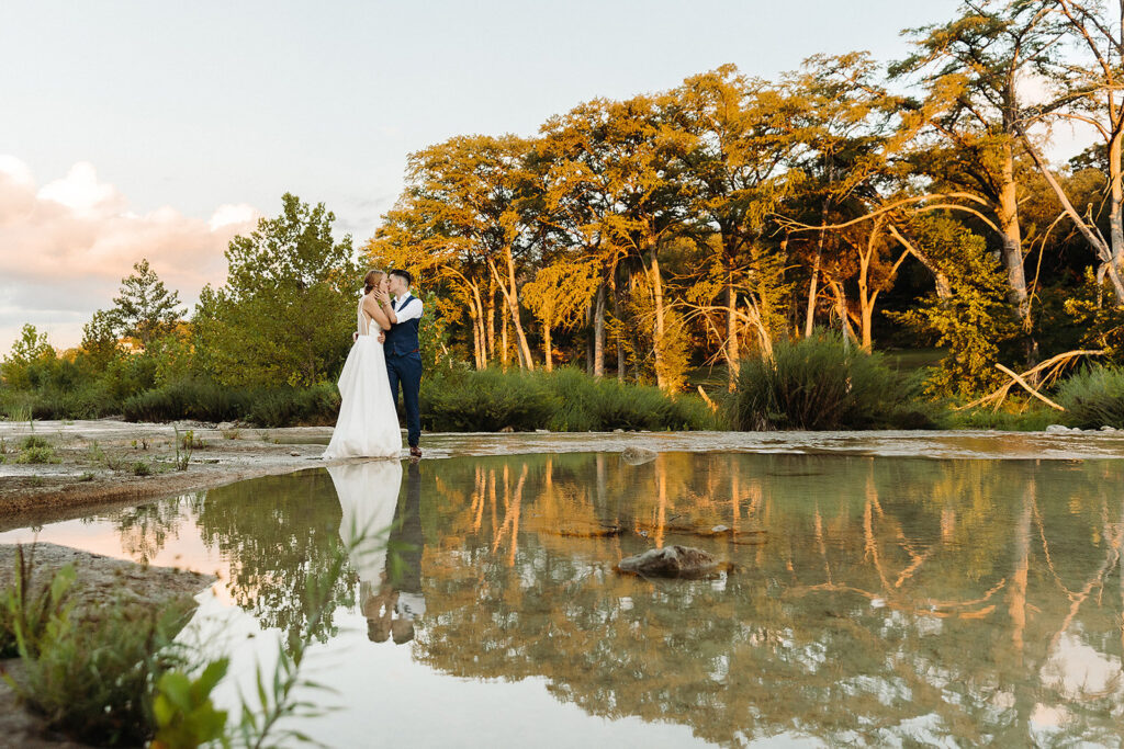 Wedding couple kissing on the edge of a river at their wedding venue.